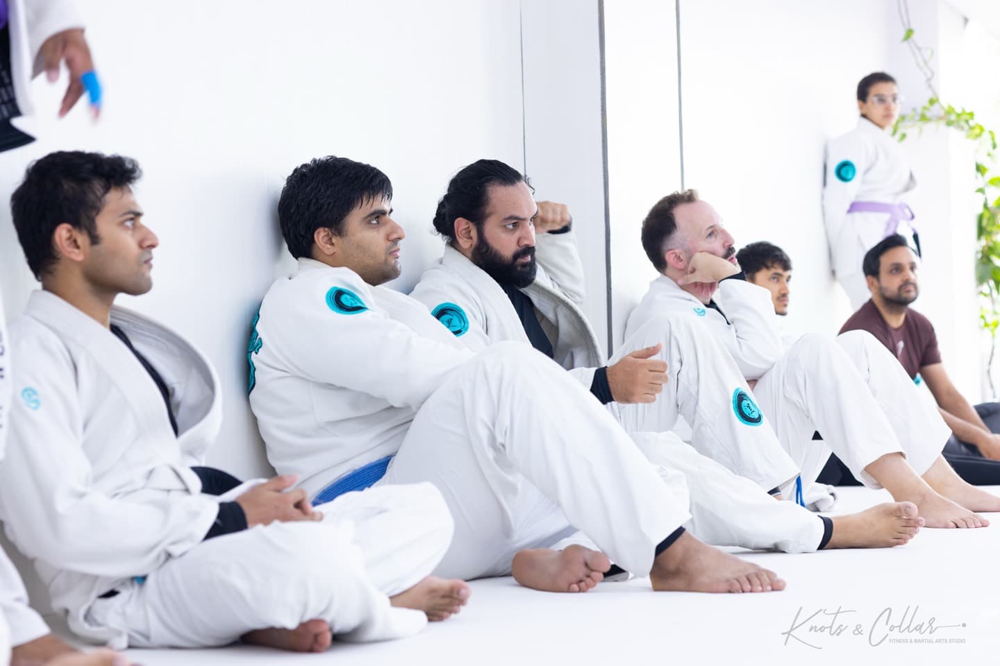Students sitting along the wall watching instruction during a jiu-jitsu class at Knots & Collar, Defence Colony